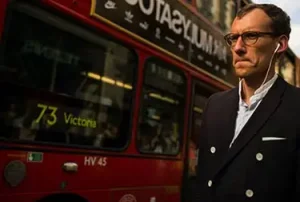 Man walking next to a bus in London, UK - CryptoLists.com London bus with a man walking